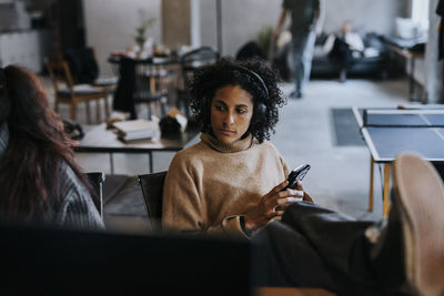 Contemplative businesswoman with smart phone sitting in creative office