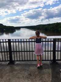 Rear view of young woman standing by railing against lake