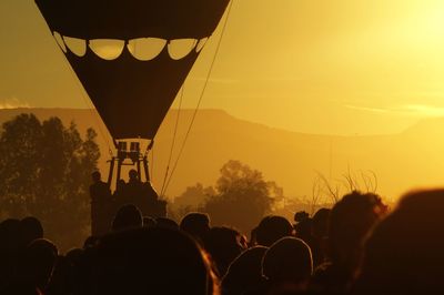 Crowd by hot air balloon during sunset
