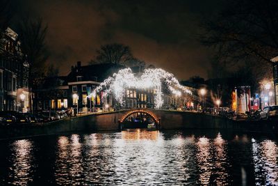 Illuminated city by river against sky at night