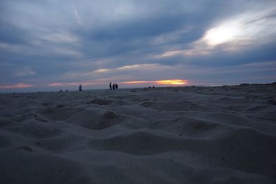 Silhouette people at sandy beach against cloudy sky during sunset