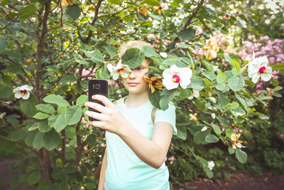 Beautiful teenager blonde girl make selfie on blooming spring magnolia trees background 