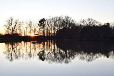 Silhouette trees by lake against sky during sunset