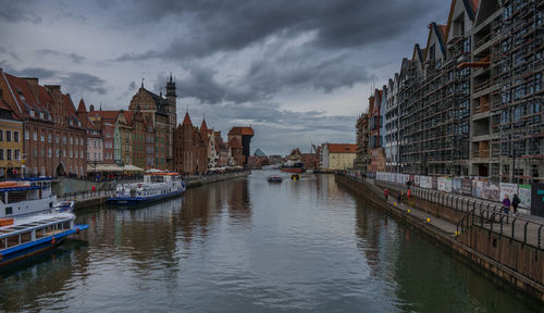 Boats moored in canal amidst buildings in city against sky