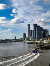 Boats in river by buildings in city against sky