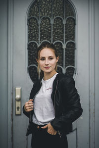 Young woman wearing leather jacket while standing by door