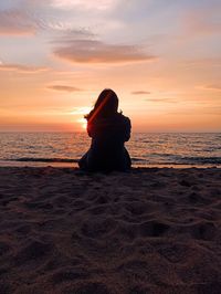 Rear view of woman sitting on beach during sunset