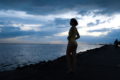 Woman standing on beach against sky during sunset