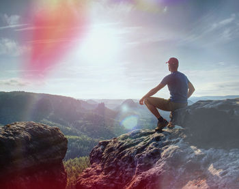 Hiker in black on the rocky peak. daybreak in mountains, mist in deep valley. man sit on the rock.