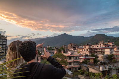 Rear view of people looking at cityscape against sky during sunset