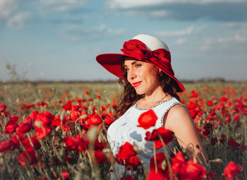 Portrait of young woman with red poppy flowers in field