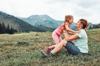 Little girl playing with her mother on grass enjoying summer day. happy family playing in the field