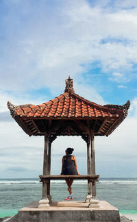 Girl sitting at temple against sky