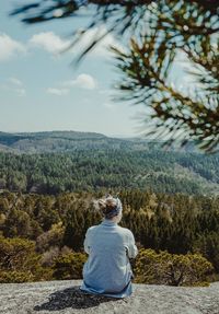 Rear view of woman sitting on rock against sky