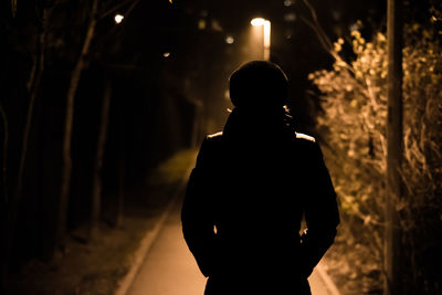 Rear view of silhouette woman standing on footpath at night