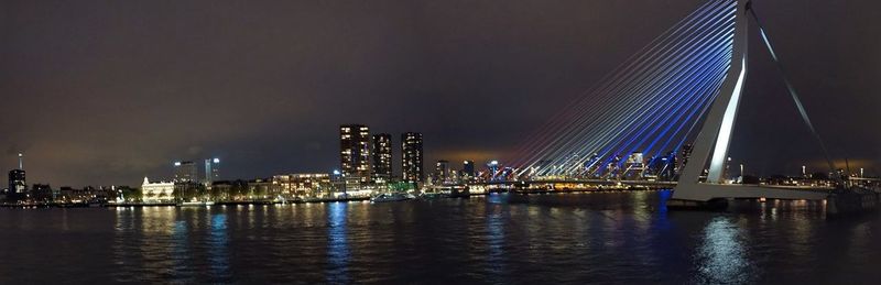 Illuminated city by river against sky at night