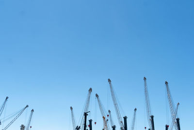 Low angle view of cranes against clear blue sky