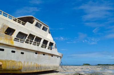 Low angle view of abandoned ship on beach against sky