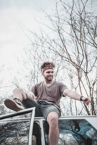 Low angle view of young man sitting on car roof