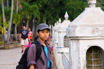 Portrait of girl with backpack standing by retaining wall