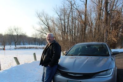 Portrait of man standing by car during winter