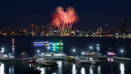 Firework display over sea against sky at night