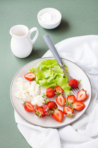 Fresh whole and sliced strawberries, cottage cheese and lettuce on a plate and sour cream in a bowl 