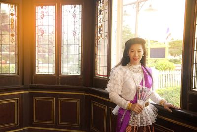 Portrait of smiling young woman in traditional clothing standing by window