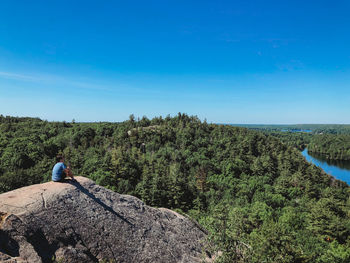 Teen boy sitting on the rocky summit of a hiking trail on a sunny day.