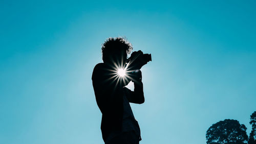 Low angle view of silhouette person against blue sky on sunny day