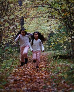 Full length of playful sisters running in forest during autumn