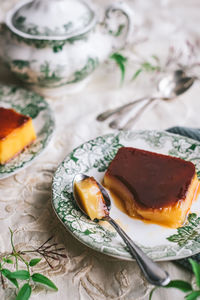 Top view of yummy caramel pudding served on ceramic plates with sauce and spoon during breakfast on table with white tablecloth