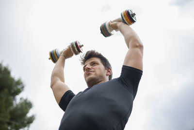 Low angle view of man holding bottle against sky