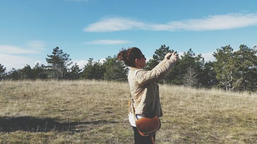 Side view of woman photographing while standing against blue sky