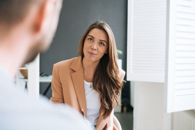 Young woman with long hair in stylish suit working with young man, woman interviews man in office