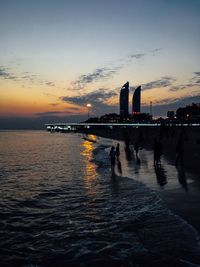 Silhouette people on sea against sky during sunset