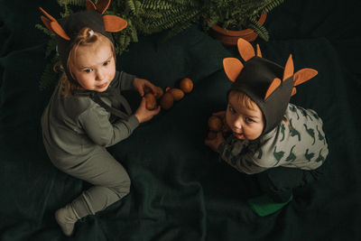 Toddler twins in funny dino costumes sitting with eggs in hands