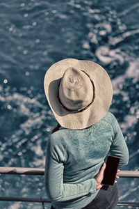 Rear view of boy holding hat sitting outdoors