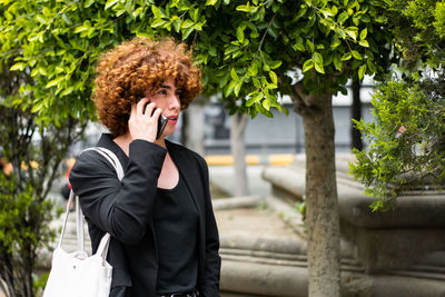 A non-binary person with a suit is talking by phone