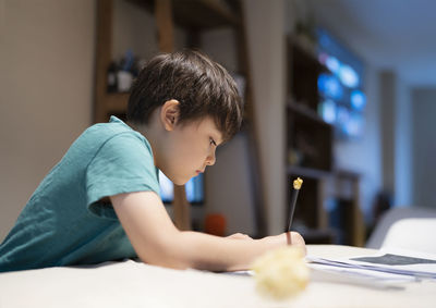 School kid boy siting on table doing homework, child boy holding pencil writing on paper