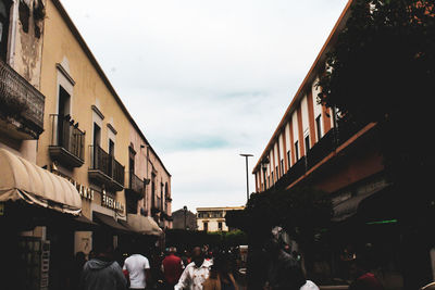 People on street amidst buildings in city against sky