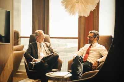 Male lawyers planning while sitting against window at legal office