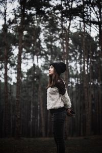 Woman looking away standing against trees in forest