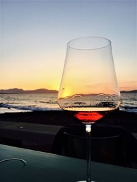 Close-up of wineglass on beach against sky during sunset