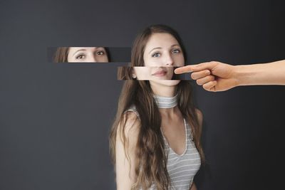 Digital composite image of hand pointing towards young woman against black background