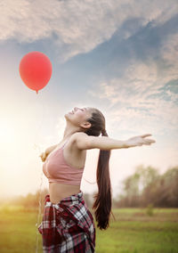 Rear view of woman standing on balloon at field against sky during sunset