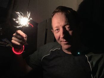 Portrait of young man holding illuminated light in the dark