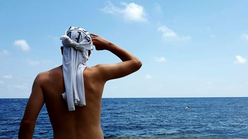 Rear view of shirtless man shielding eyes against sea