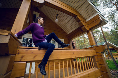 Young woman in a purple sweater and black jeans out on the porch of a wooden house