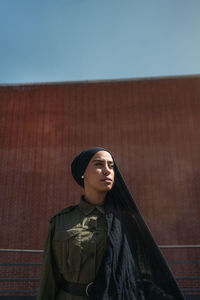 Portrait of young woman standing against wall